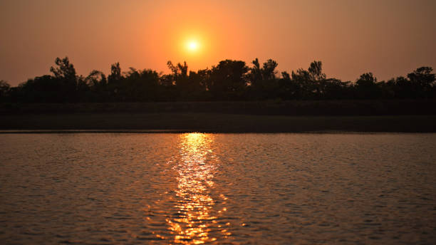 This scene captures the breathtaking reflection of a sunset on a tranquil lake, framed by a vibrant orange sky.  The peaceful atmosphere, enhanced by the warm colors of the sky, highlights the natural beauty and tranquility of the scene. This scene perfectly encapsulates the serene and captivating essence of a sunset over a calm lake.