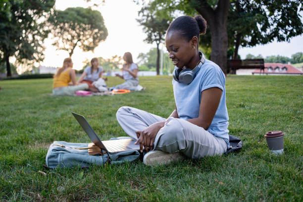 istock Young female black ethnicity university student studying on a laptop while sitting on the grass in a campus park 2159914405