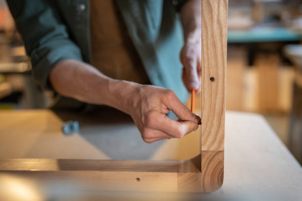 Male craftsman screwing furniture screws into the table, joins the pieces together, hands using hex wrench closeup. Creating furniture for home, customised work. Carpentry workshop.