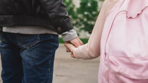 istock Back to school. Schoolgirl with backpack and father going to school first lesson holding hands back view close up. Man dad and daughter kid walking outdoor schoolyard 2159919476