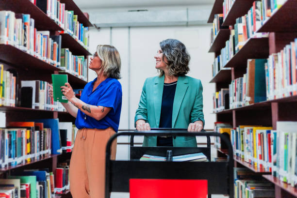 istock Mature librarians keeping books on the shelf at library 2159920040