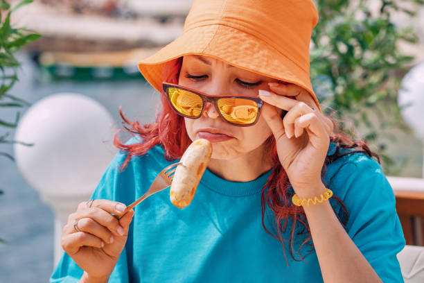 A person making a disgusted face while looking at spoiled sausage, expressing concern over its bad odor and potential bacteria.