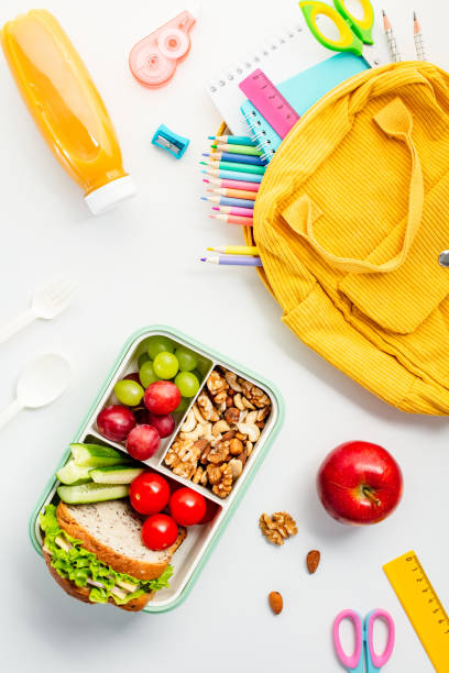 istock Nutritious lunchbox with fruit, vegetables, nuts and educational supplies on a white background. Flat lay, top view. 2159920341