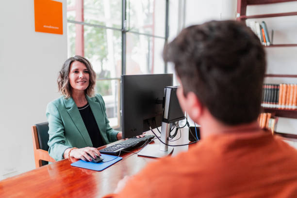 istock Mature librarian woman using laptop and talking to customer at library 2159920540