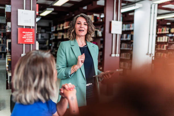 istock Mature teacher woman talking to students on at library 2159920587