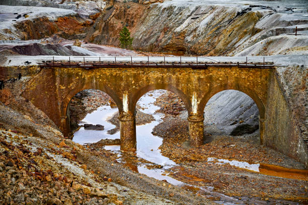 An old arch bridge crosses over a stream tinged with the reddish hues of pollution in the Rio Tinto mining area