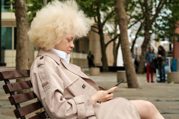 istock Albino woman sitting on a bench reading an e-book. 2159930632