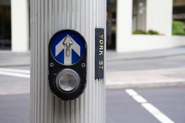 At a bustling intersection, a pedestrian crossing button adorned with a prominent arrow provides essential guidance and safety for pedestrians navigating the urban environment. Positioned strategically to assist in crossing the street safely, it serves as a vital tool for managing the flow of foot traffic amidst the bustling cityscape. As pedestrians approach, they rely on the button to activate traffic signals, halting vehicles and signaling the right-of-way to cross. This scene exemplifies the harmonious interaction between technology and urban planning, ensuring efficient and safe pedestrian movement in a dynamic and vibrant city setting.