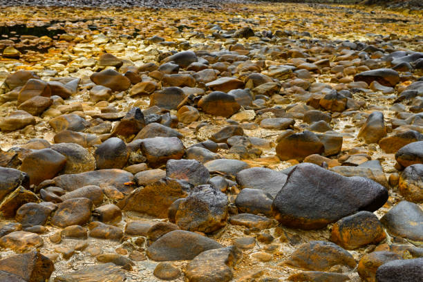 A close view of the yellowish, sulfur-covered rocks in the riverbed of Rio Tinto under a hazy sky
