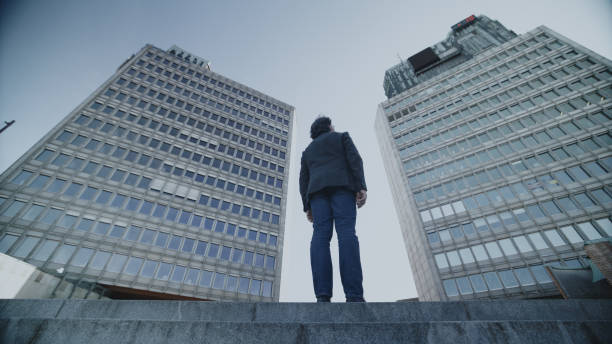 A senior man in casual attire strolls near towering office buildings, signaling a blend of active aging and modern work environments.