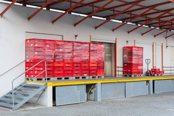 istock Stacks of red plastic crates wrapped in polythene stand on pallets on a warehouse loading dock. 2159942682