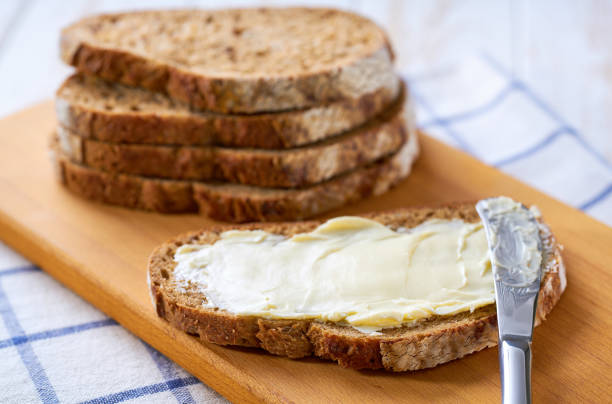 istock Tasty cut multigrain sourdough bread with fresh butter on a white wooden table. 2159951621
