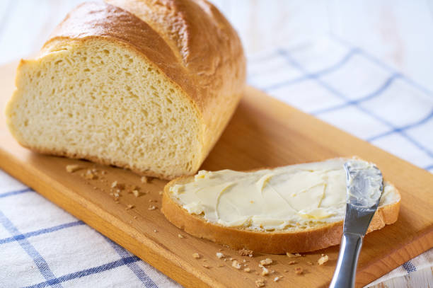 istock spreading butter in to white wheat bread slices on a light kitchen table. 2159951624