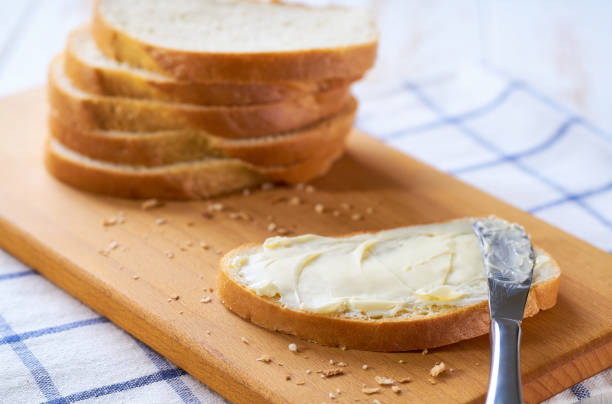 istock knife spreading butter on wheat bread slices on a white wooden table. 2159951647