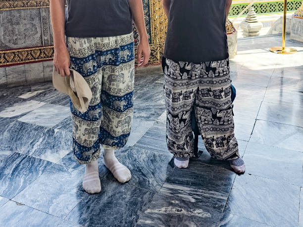 Two tourists unrecognisable wearing elephant-patterned trousers at a Thai temple. These famous trousers are sold at the entrances to temples. The temples are not accessible in trousers or short skirts.