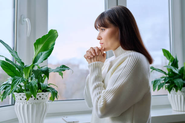 Serious thoughtful middle aged female looking out the window at home