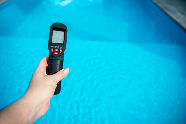 Hand holding digital infrared thermometer, measuring temperature of swimming pool. Water quality and inspecting chlorine capacity with remote controller. Copy space