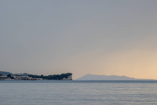 Calm sea during a sunset in the late spring. Resort in Roda and cliffs beside. Cloudy sky. Island Othonoi on the horizon. Acharavi, Korfu, Greece.