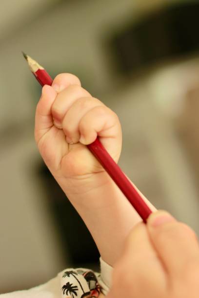 A close-up of a child’s hands using a blue pencil to draw on paper. The robot illustration is in progress, featuring detailed lines and elements