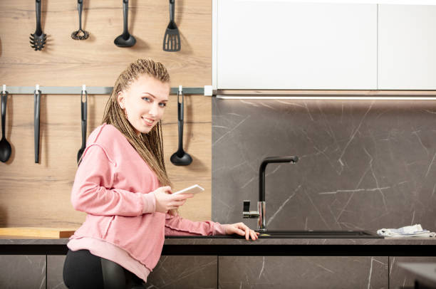 istock Young woman using smartphone and smiling in modern kitchen 2160000518