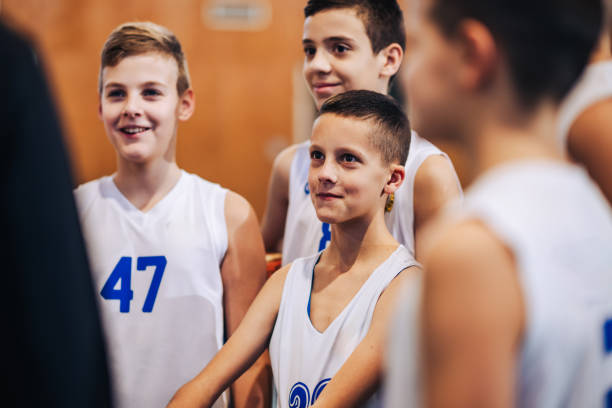 Smiling young basketball players listen to their coach in a cheerful atmosphere during a sport session inside a gym