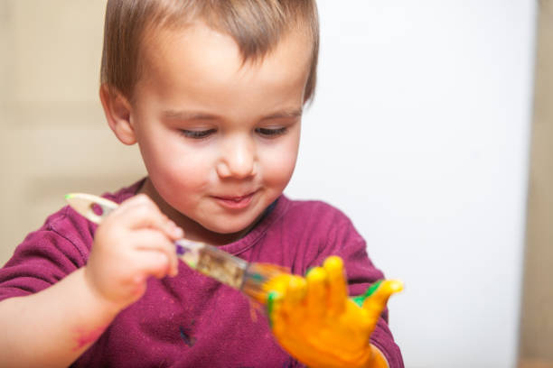 Kid painting his hand with a brush and colored paint. Playful activity.