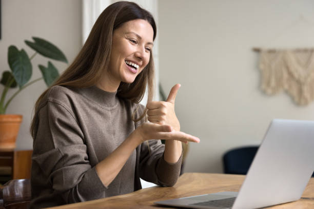 Happy communication expert speaking to patient with hearing disability online Happy communication expert speaking to patient with hearing disability online, showing thumb up on palm at computer, smiling, laughing. Sign language therapist using Internet for communication sign language stock pictures, royalty-free photos & images
