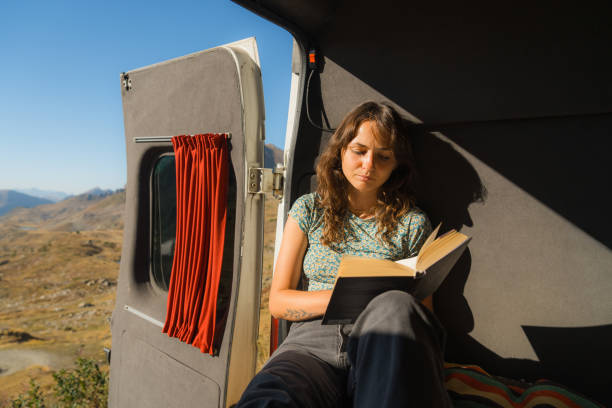 istock Woman reading book in camper van in mountains 2160018528