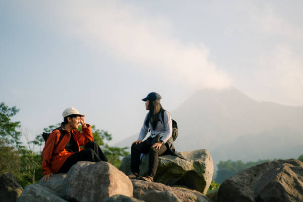 istock Two Friends Hanging Out Resting on Large Rocks with Merapi Mountain at the Background 2160021367