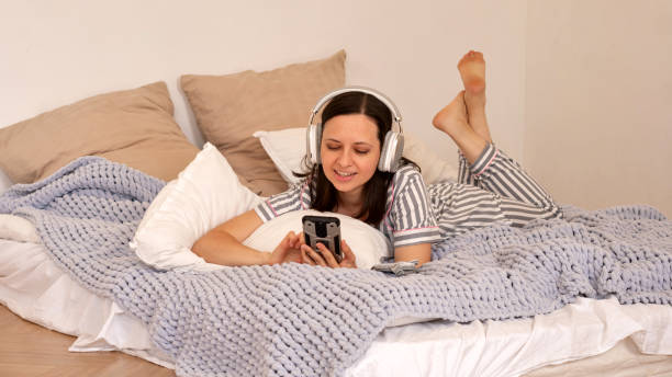 istock Woman lying in bed with headphones, using smartphone. 2160023700