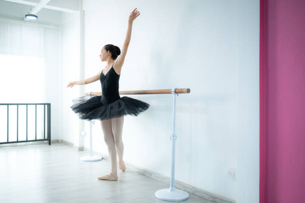 A girl ballet student practices ballet dancing at home with a white background