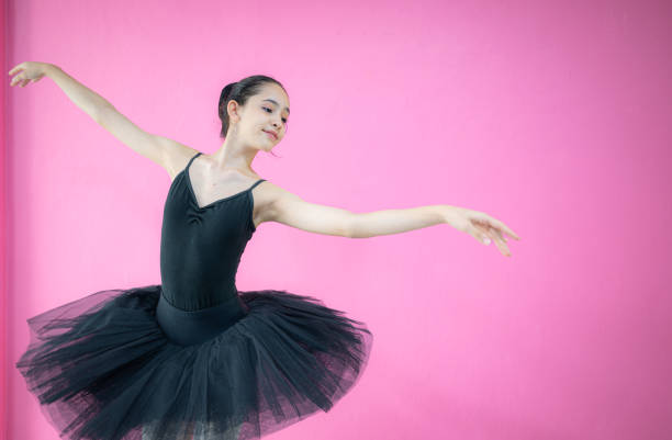 A girl ballet student practices ballet dancing at home with a white background