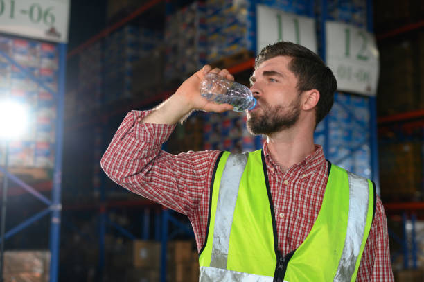 istock Time of rest from work. Tired warehouse employees man drinking water and resting after working at warehouse factory workplace. 2160035728