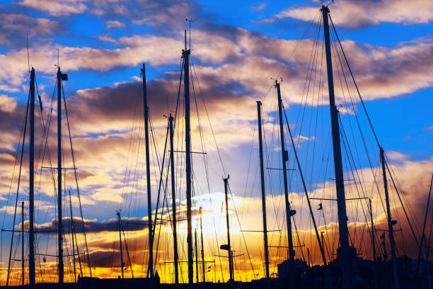 Sailboats moored at a harbor as the twilight. Silhouette of yachts in the port at sunset. Group of sailboats are lined up in a marina, with the sun setting in the background