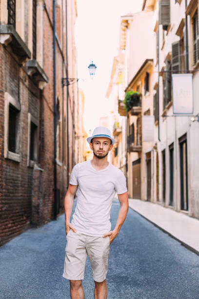 guy with a stylish beard in white clothes and boater hold hands in pockets. guy on the streets of the city