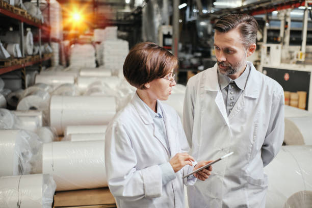 istock Two factory workers in white robe with tablet standing in the warehouse 2160037772