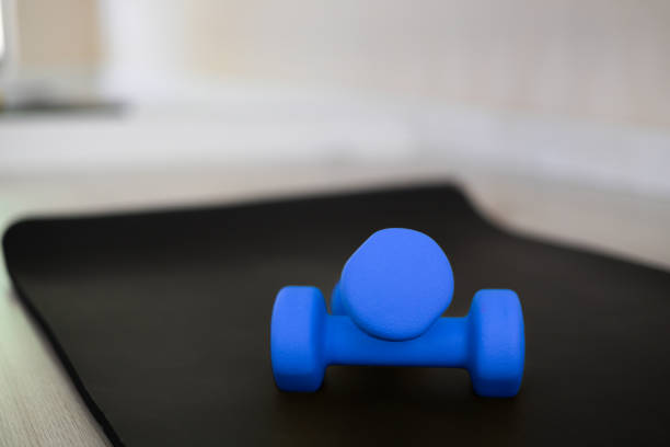 Close-up with blurred background blue dumbbells on a black yoga mat in light beautiful sport studio, fitness and gym