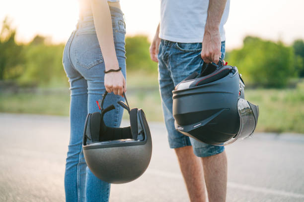 Two young people are standing next to a motorcycle, holding helmets.