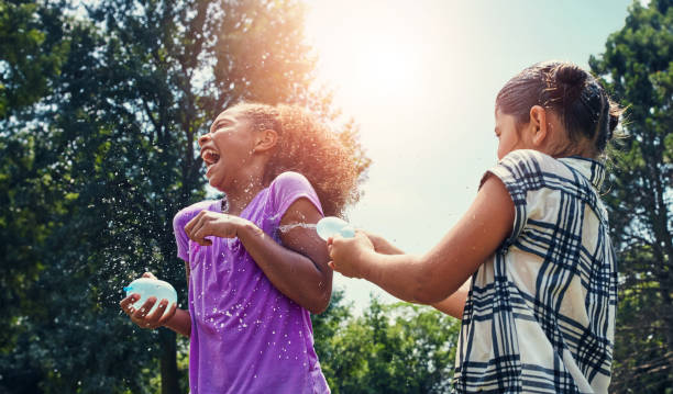 Children, energy and water balloon for friends in a park with splash fun, playing and bonding in nature. Freedom, happy and girl kids in backyard with liquid bomb, games and summer vacation adventure Hot summer days deserve a water balloon fight water balloon stock pictures, royalty-free photos & images
