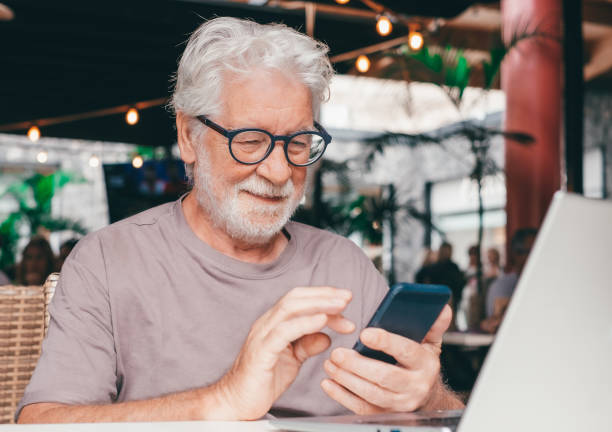 istock Attractive senior man sitting in a cafe smiling while using mobile phone. Cheerful senior male, using modern technology expressing happiness and contentment in a relaxed atmosphere 2160049798