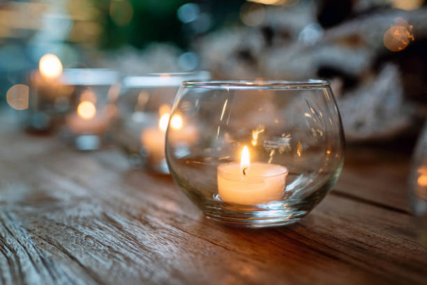 Row of glass bowls with burning candles placed on wooden table against blurred background