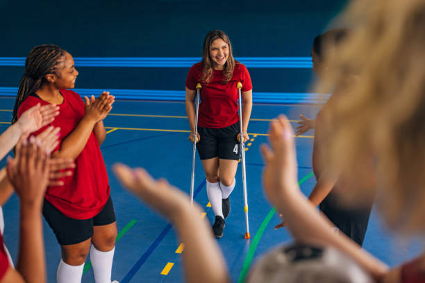istock Female athlete on crutches with team cheering around 2160055037