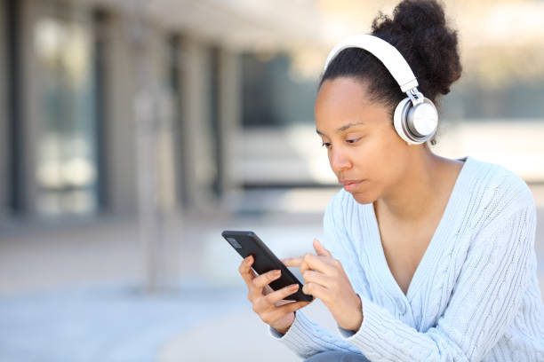 istock Black woman wearing headphone checking phone 2160056089