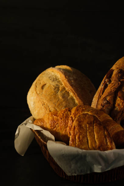 Rustic crusty loaves of bread with grain in wicker basket on rustic wooden table.