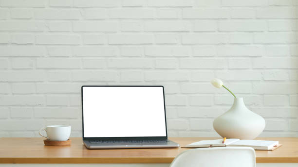 istock Laptop with empty screen, coffee cup and modern ceramic vase on wooden table against brick wall. 2160059683