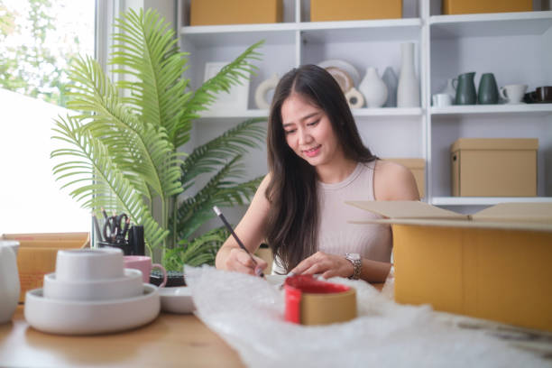 istock Small business entrepreneur writing order in notebook while sitting in pottery shop with handmade ceramic products. 2160060001
