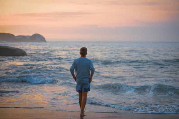 istock A teenage boy walks alone on the beach during sunset. 2160061238