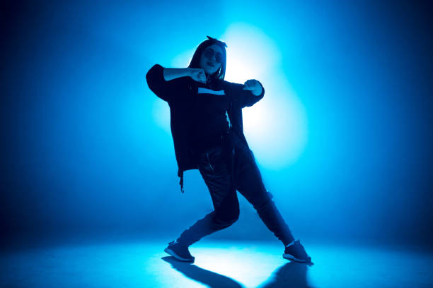 istock Young woman hip-hop dancer on studio blue light background with flare effects 2160066441