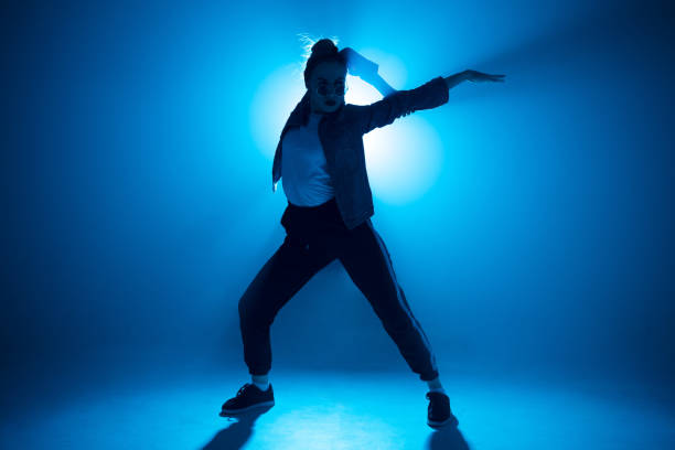 istock Young woman hip-hop dancer on studio blue light background with flare effects 2160066446