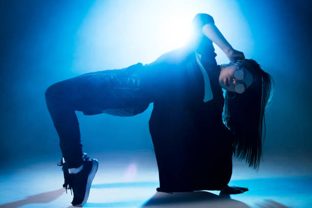 istock Young woman hip-hop dancer on studio blue light background with flare effects 2160066470